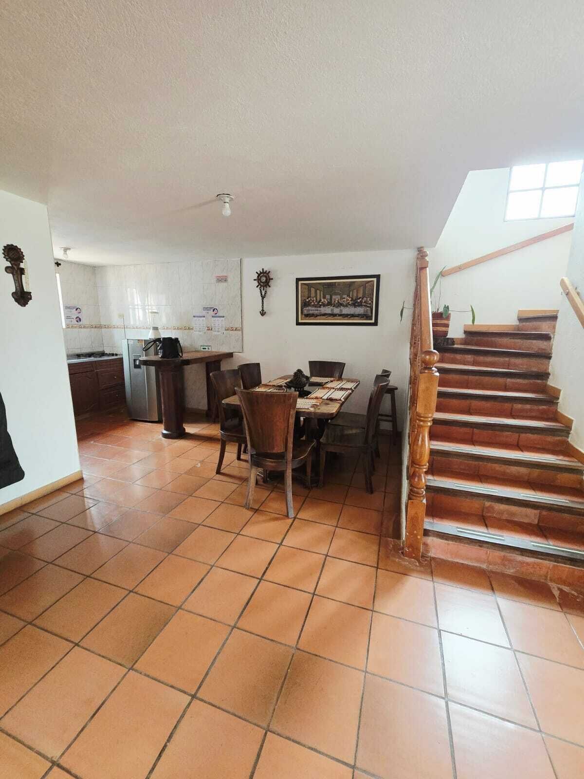 A spacious living area with a dining table, chairs, a kitchen area, and a wooden staircase.