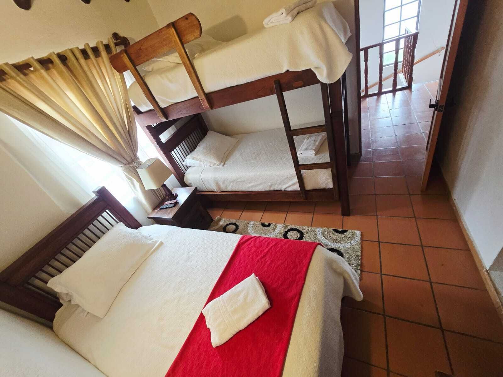 A room with two bunk beds, a small table with a lamp, and a window with curtains.
