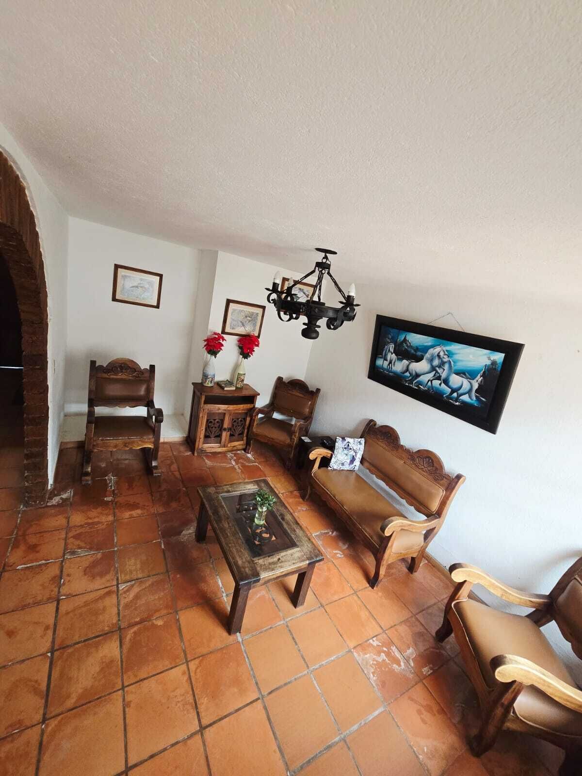 A cozy living room with a tiled floor, wooden furniture, a chandelier, and a framed picture on the wall.