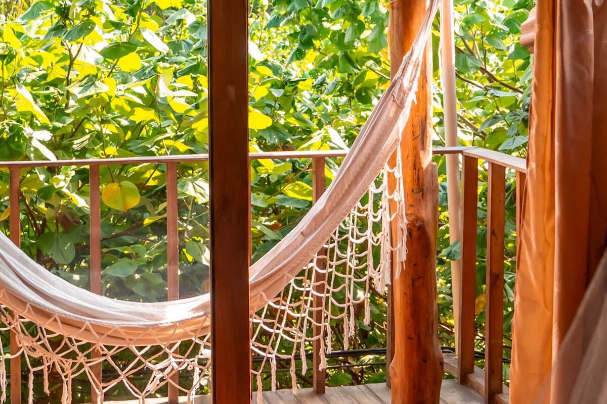 A wooden deck with a hammock and a view of lush green foliage.