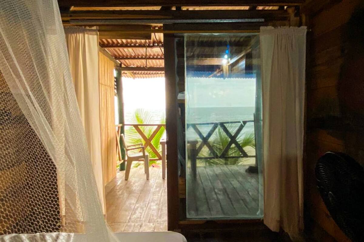 A room with a bed, a view of the sea through a glass door, and a wooden deck outside.
