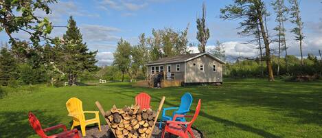 A backyard with a fire pit, colorful Adirondack chairs, and a wooden deck leading to a house.