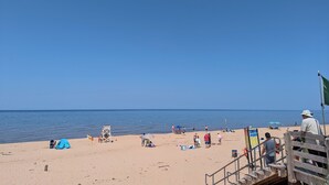 Una playa con una escalera de madera que baja a la arena, una torre de salvavidas y una carpa montada en la playa.