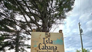 Un letrero de madera indica Isla Cabana Upcountry Stay, rodeado de árboles y una mesa de picnic.