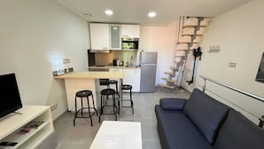Un ambiente compatto con angolo cottura, divano, tavolino e televisione.