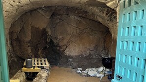 Un tunnel in pietra ad arco, stretto, con pavimento in cemento, una panchina in metallo e una griglia.