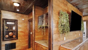 Een houten interieur met een inbouwkast die decoratieve objecten toont, een aan de muur bevestigde televisie en een hangplant.