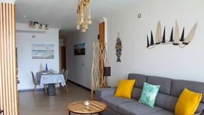 Un salon moderne avec un canapé gris, des coussins jaunes, une table basse ronde en bois et un coin repas comprenant une table et des chaises.