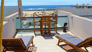 Un balcon avec une table et des chaises, donnant sur une plage et l’océan.