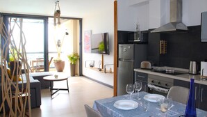 Une cuisine moderne équipée d’un four, d’un micro-ondes et d’une cuisinière encastrés. On y trouve un coin repas avec une table pour deux, et un téléviseur fixé au mur.
