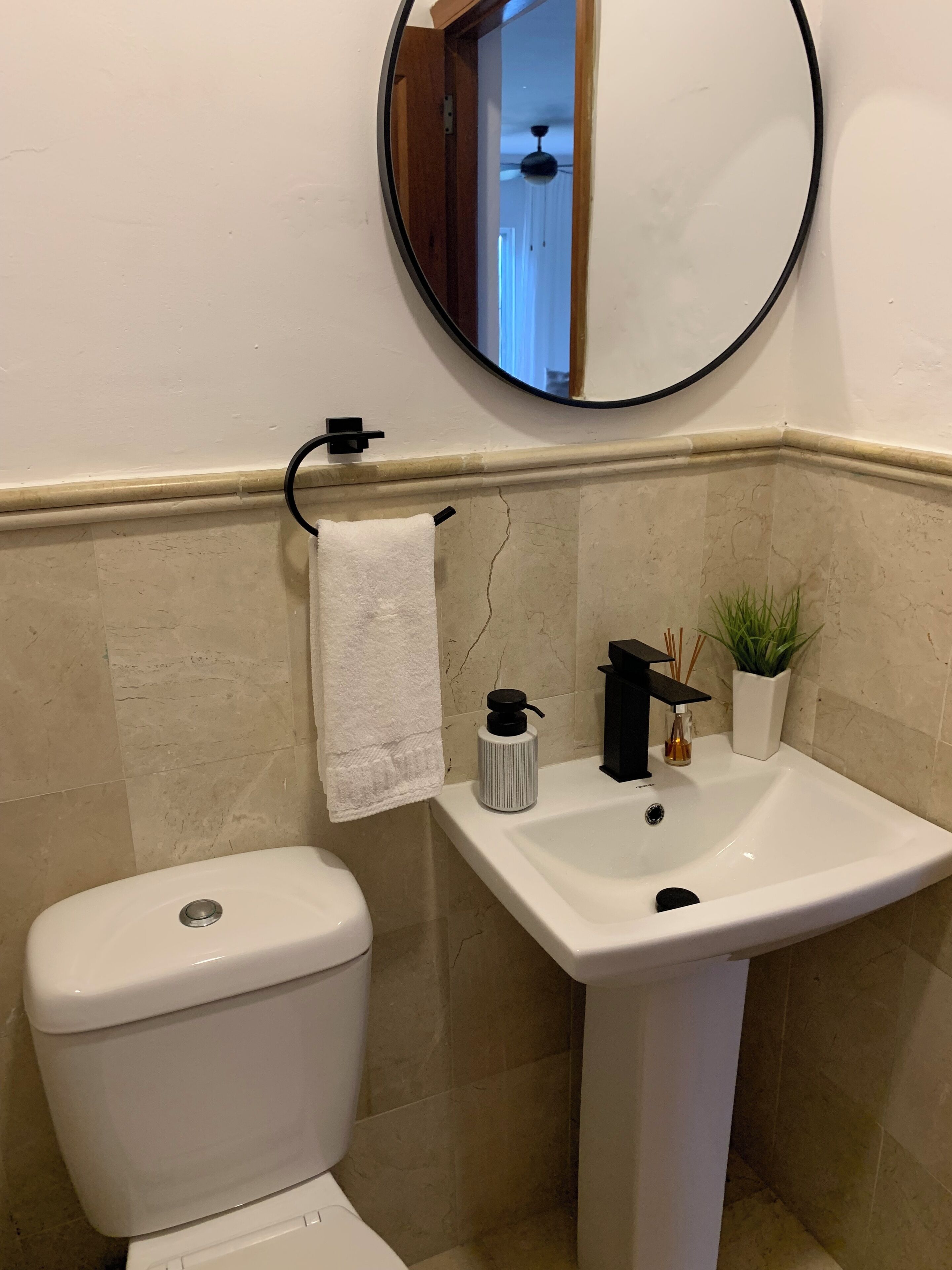 A bathroom with a white toilet, a sink with a black faucet, a towel hanging on a rack, a potted plant, and a mirror on the wall.