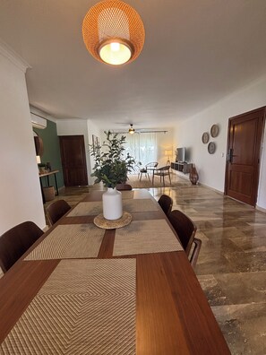 Un comedor con una mesa de madera, individuales tejidos y una planta en maceta.