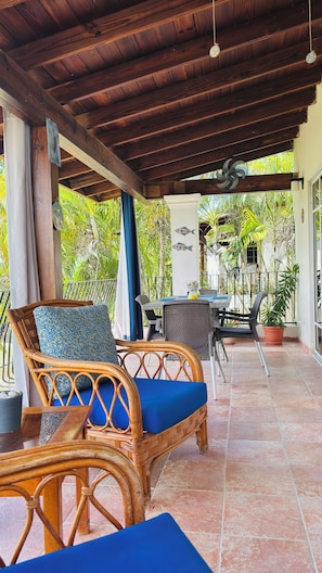 A covered outdoor seating area with wicker furniture and a tiled floor.