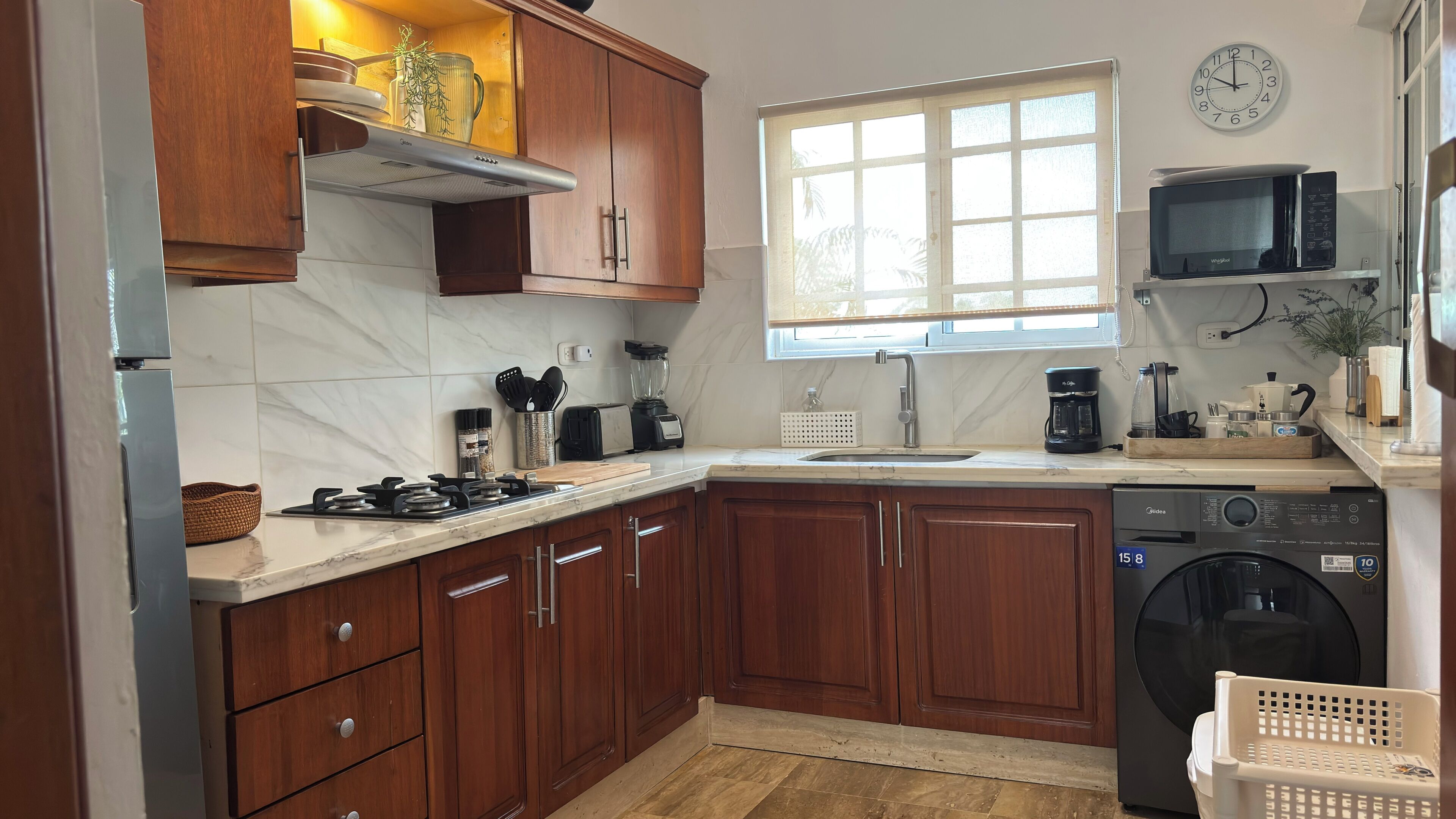 Una cocina con armarios de madera, estufa, microondas, pileta y lavavajillas.