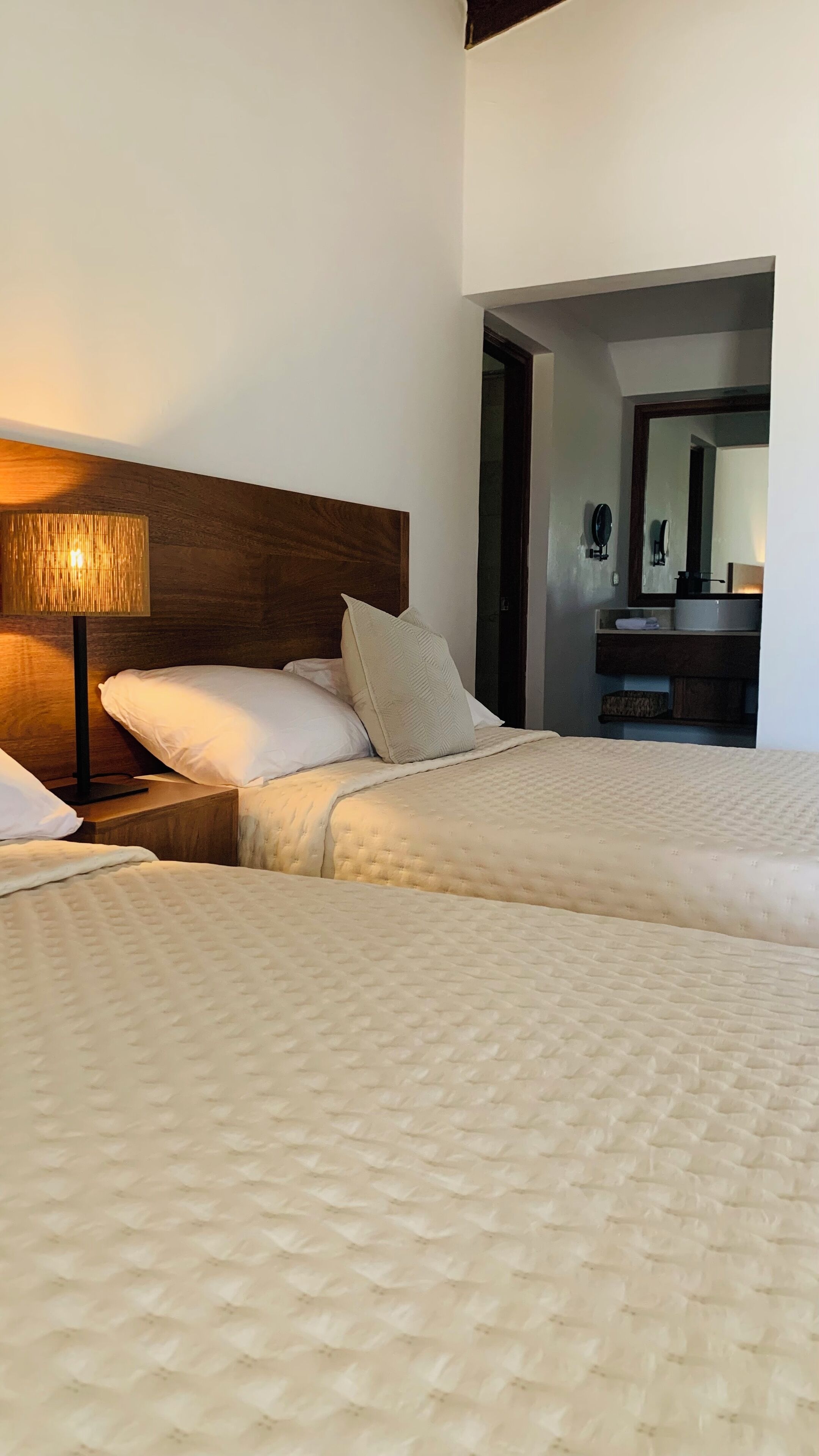 Une chambre d’hôtel avec deux lits, une tête de lit en bois, une lampe de chevet et un miroir au mur.