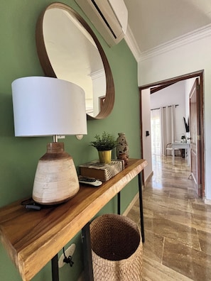 A wooden console table with a lamp, a potted plant, a book, a vase, and a remote control.