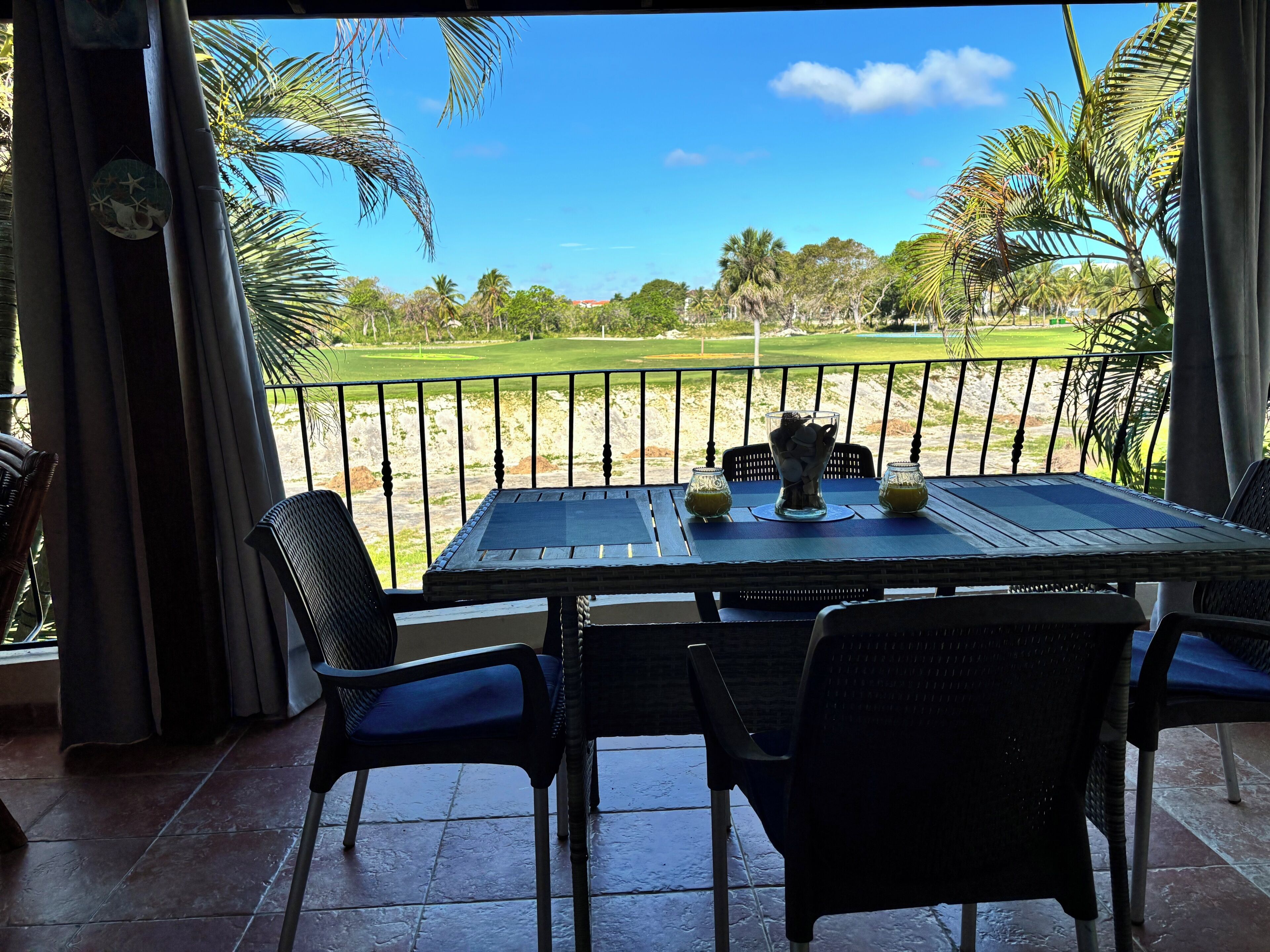 A table with chairs on a balcony overlooking a golf course.