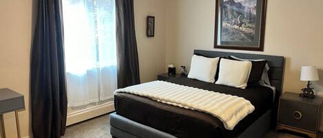 A bedroom with a bed, a nightstand, a lamp, a ceiling fan, and a window with curtains.