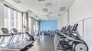 Een sportschool met loopbanden en fitnessapparatuur, grote ramen en een blauwe muur.