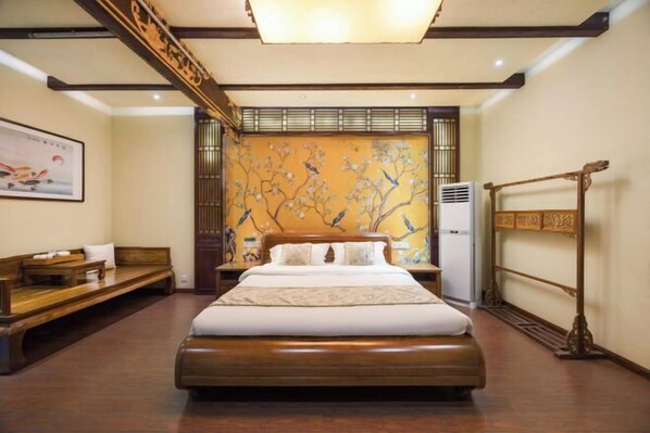 Un dormitorio con una cama grande, un banco de madera, un aire acondicionado montado en la pared y un adorno mural de estilo tradicional.