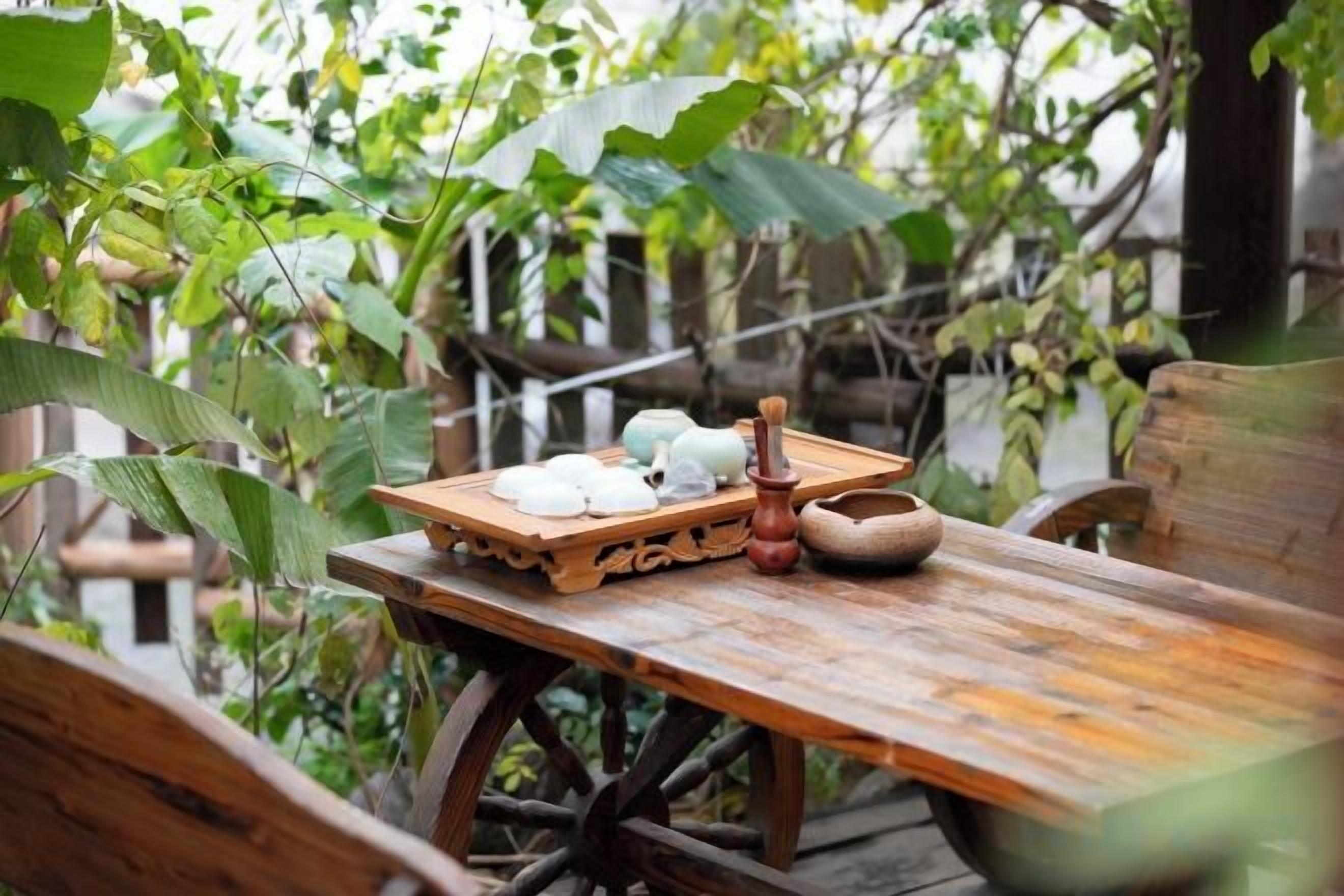 A rustic wooden table with a tray of food and a bowl, set outdoors with greenery in the background.