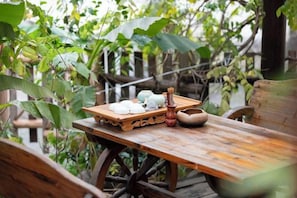 Una mesa de madera rústica con una bandeja de comida y un bol, dispuesta al aire libre con follaje de fondo.