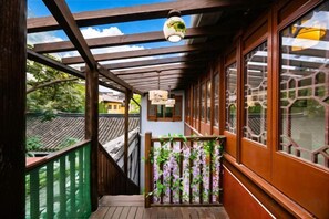 Un balcón de madera con vistas a edificios tradicionales, una lámpara colgante y una barandilla verde.