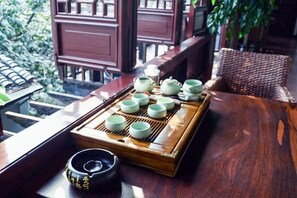 Un juego de té tradicional sobre una bandeja de madera, con varias tazas y una tetera, colocado sobre una mesa con vista a un edificio tradicional y vegetación exterior.