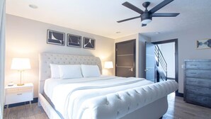 Une chambre à coucher moderne avec un grand lit, deux tables de chevet avec des lampes, un ventilateur de plafond et une armoire.