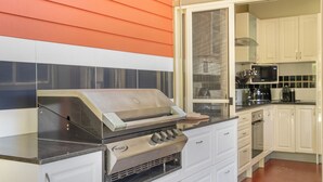 Een keuken met een ingebouwde gasgrill, witte kastjes en een raam met uitzicht op de achtertuin.