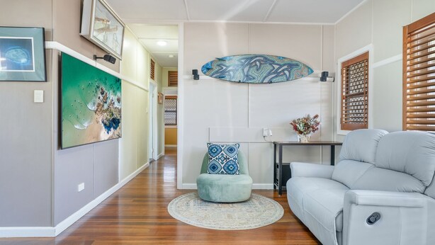 Een moderne woonkamer met een witte bank, een rond vloerkleed en een aan de muur bevestigd surfboard.