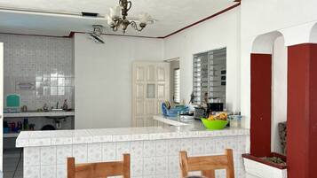 Une cuisine avec des carreaux blancs, un coin repas avec une table et des chaises, et un ventilateur de plafond.