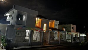 A modern two-story house with a gated entrance, illuminated windows, and a visible moon in the sky. - TREEBU HOSTEL (Valladolid)