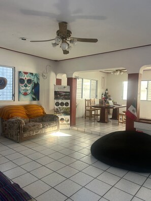 A living room with a sofa, a black bean bag, a ceiling fan, and a mural on the wall. - TREEBU HOSTEL (Valladolid)