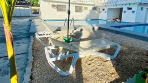 An outdoor pool area with a white umbrella, lounge chairs, and a building in the background. - TREEBU HOSTEL (Valladolid)