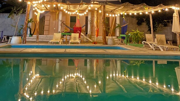 A pool area with string lights, a covered seating area, and a reflection in the water. - TREEBU HOSTEL (Valladolid)