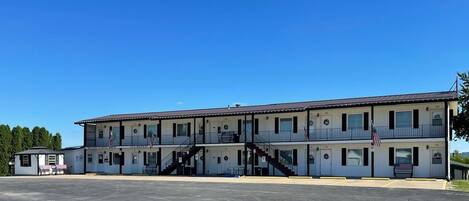 A two-story motel with a central staircase, American flags, and a parking lot.