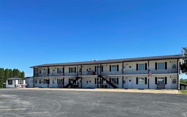 A two-story motel with a central staircase, American flags, and a parking lot. - Motel Tipton (Tipton)