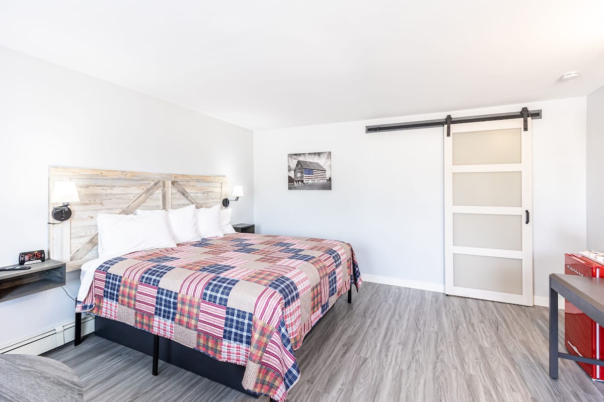 A bedroom with a bed, a nightstand, a lamp, a wall-mounted shelf, a sliding door, and a small table.