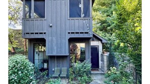 A two-story wooden house with a balcony, a front door, and a small garden area with a bench. - Modern Douglas Hideaway | Hot Tub & Patio (Douglas)