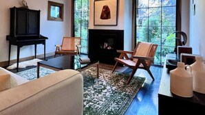 A living room with a fireplace, two armchairs, a sofa, and a coffee table. There is a large window with a view of trees. - Modern Douglas Hideaway | Hot Tub & Patio (Douglas)