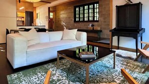 A living room with a sofa, coffee table, and patterned rug. There is a kitchen area with a dining table and chairs visible in the background. - Modern Douglas Hideaway | Hot Tub & Patio (Douglas)