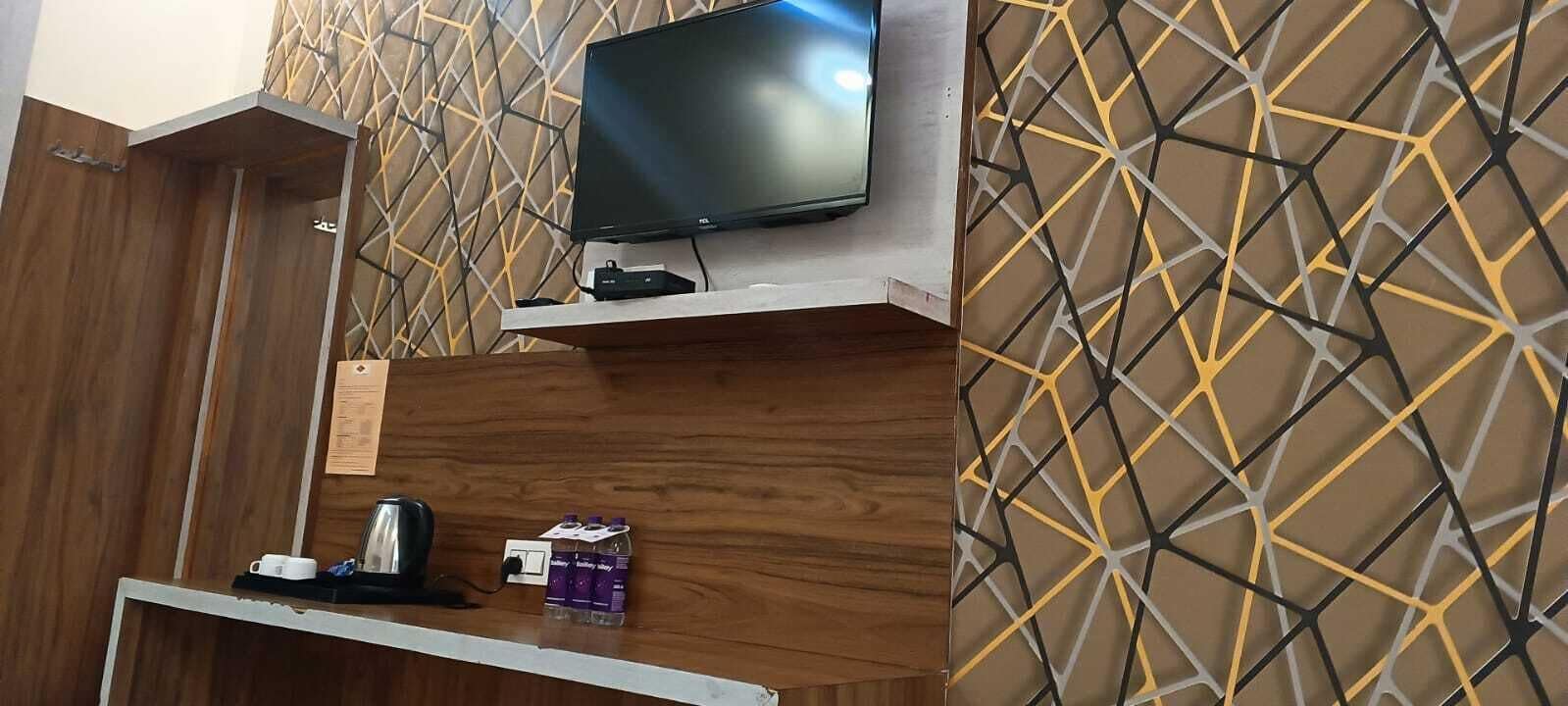 A hotel room with a flat-screen TV mounted on the wall, a wooden door, and a patterned wall.