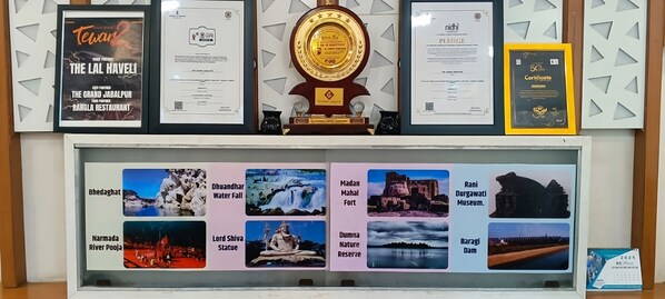 A display of various awards and certificates, including a large golden award, framed documents, and a certificate holder. - THE GRAND  (Jabalpur)