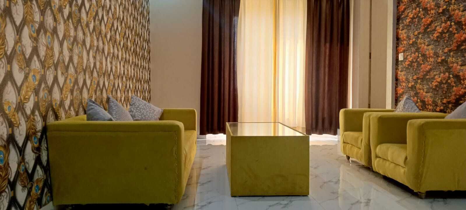 A room with two yellow sofas, a glass coffee table, and a patterned wallpaper.