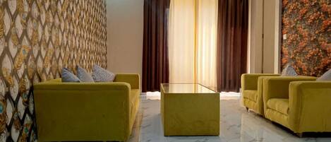 A room with two yellow sofas, a glass coffee table, and a patterned wallpaper.