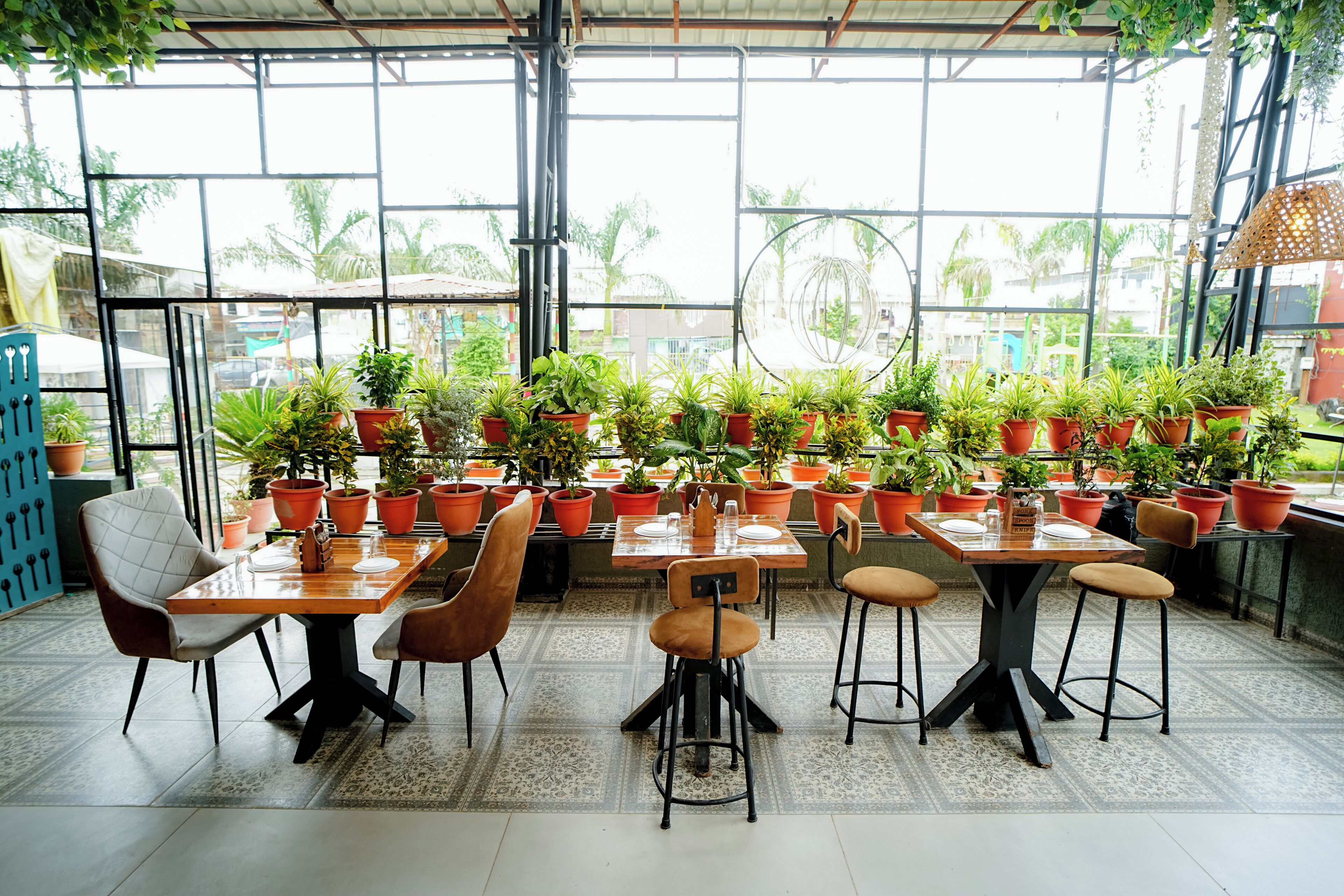 An indoor dining area with multiple tables and chairs, surrounded by potted plants.