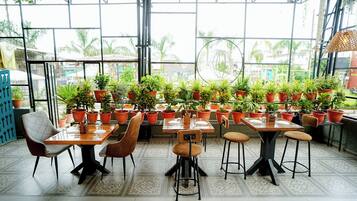 An indoor dining area with multiple tables and chairs, surrounded by potted plants.