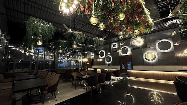 Un interior de restaurante moderno con techos altos, plantas colgantes y decoraciones circulares en las paredes.