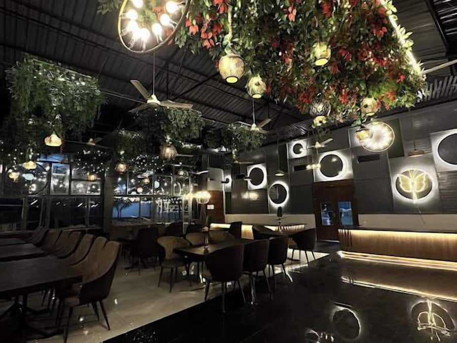 Interior moderno de restaurante com tetos altos, plantas penduradas e decorações circulares nas paredes.